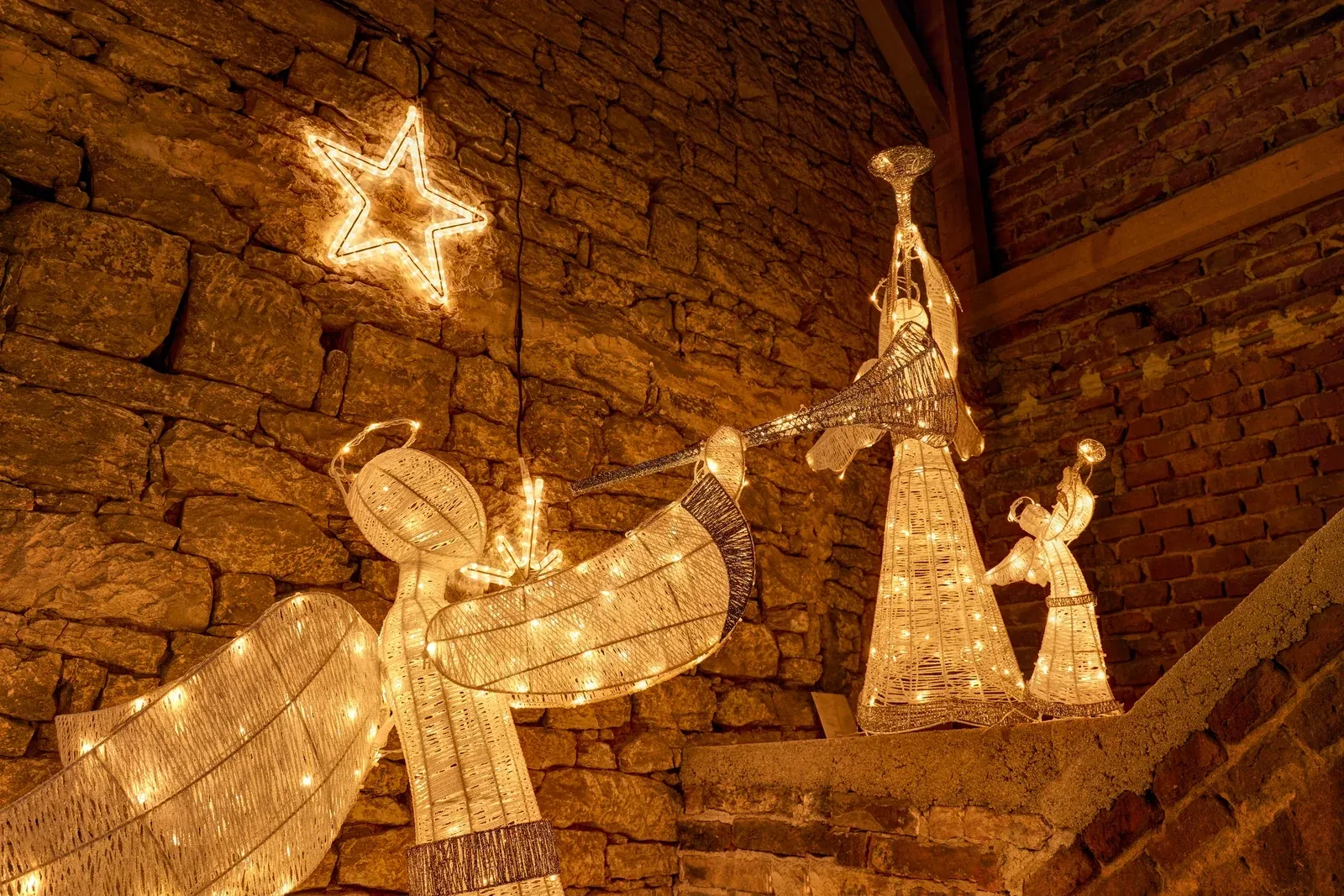 Warm white LED angel with a trumpet, 122 cm, next to a glowing reindeer and a tree with stars, a winter scene by a wall