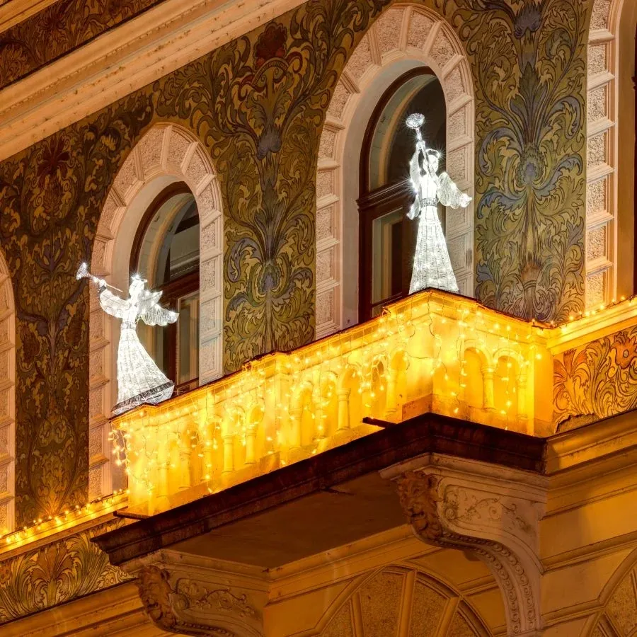 Ice white LED angels with trumpets on the balcony of a historic facade with warm white light icicles