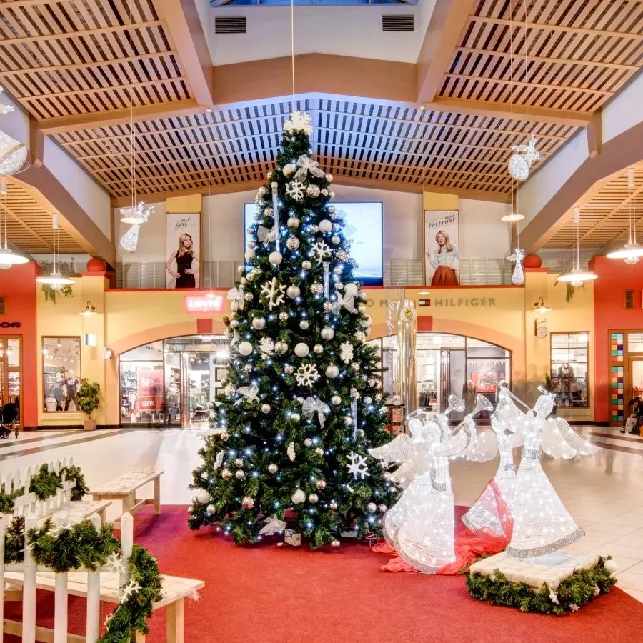 Ice white light-up angels with trumpets next to a Christmas tree in a shopping centre arcade, a photo corner